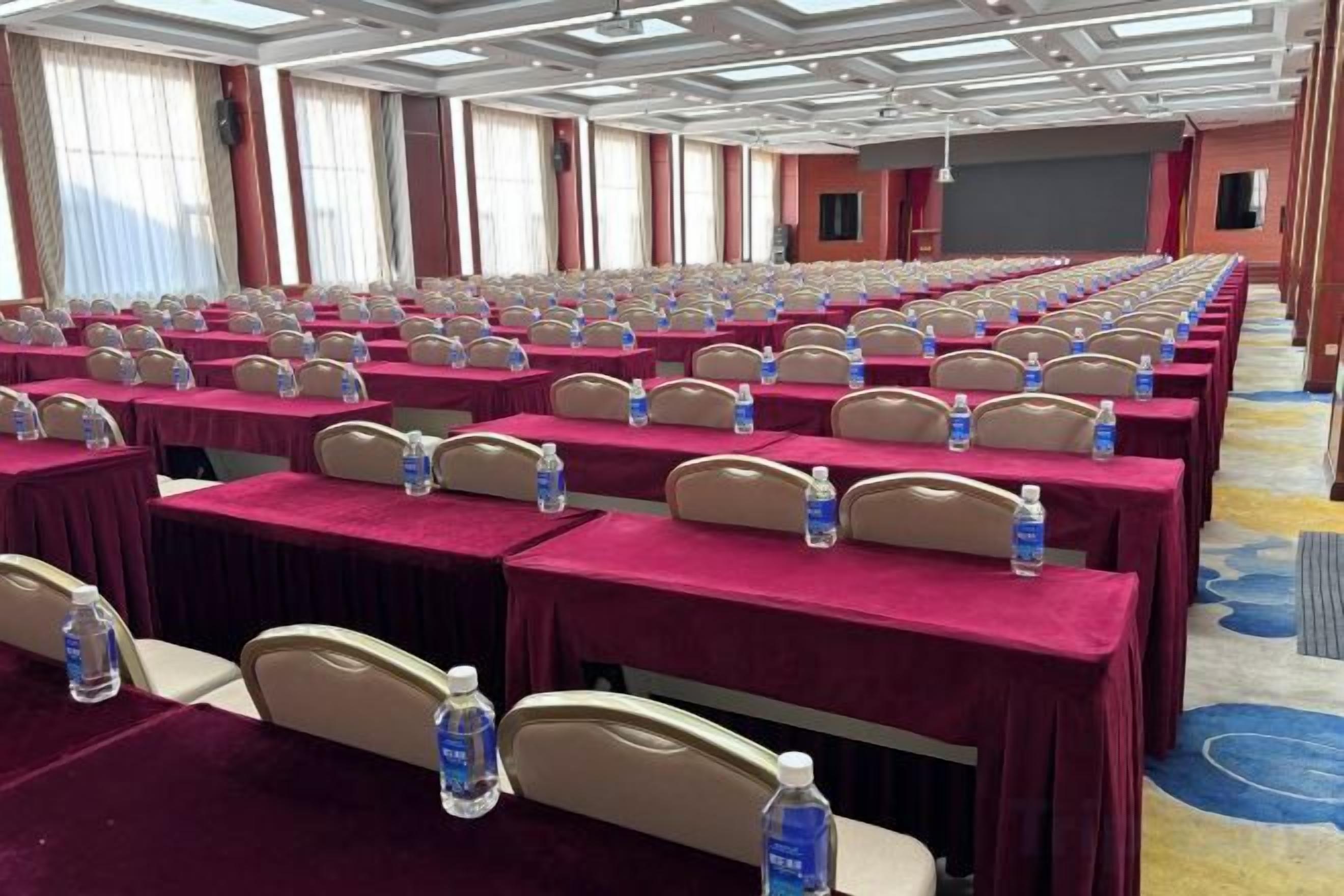 A conference room with rows of tables, each with a water bottle and a headrest.