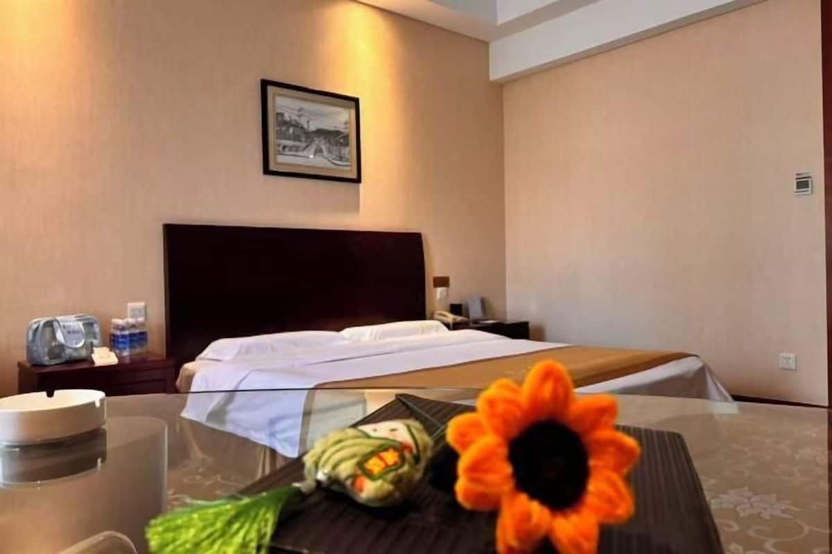 Habitació d'hotel amb un llit, una taula de nit, un quadre al mur i una taula amb una flor i una ampolla.