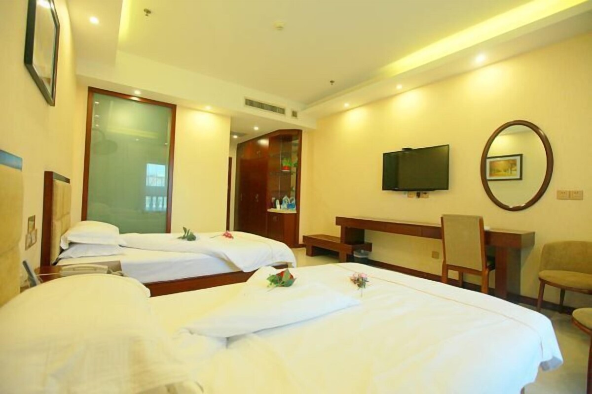 A hotel room with two beds, a desk, a chair, a television, and a mirror.
