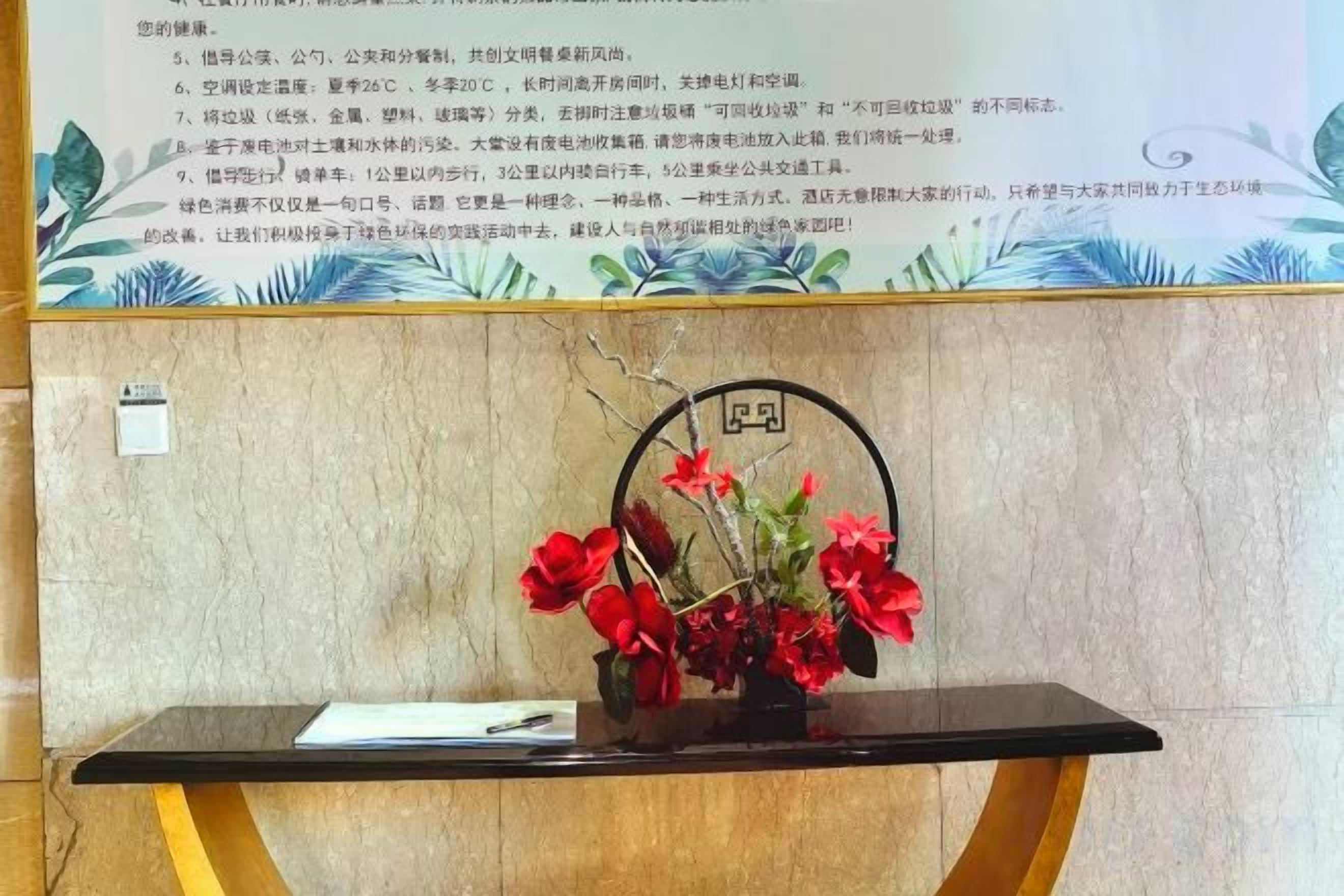 A reception desk with a vase of red flowers, a framed sign with a number, and a wall with a decorative pattern.