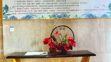 A reception desk with a vase of red flowers, a framed sign with a number, and a wall with a decorative pattern.
