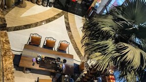A high-ceilinged lobby with a central seating area featuring a wooden table and chairs, surrounded by a palm tree and a large mirror. - Xishan Hotel (Taiyuan)