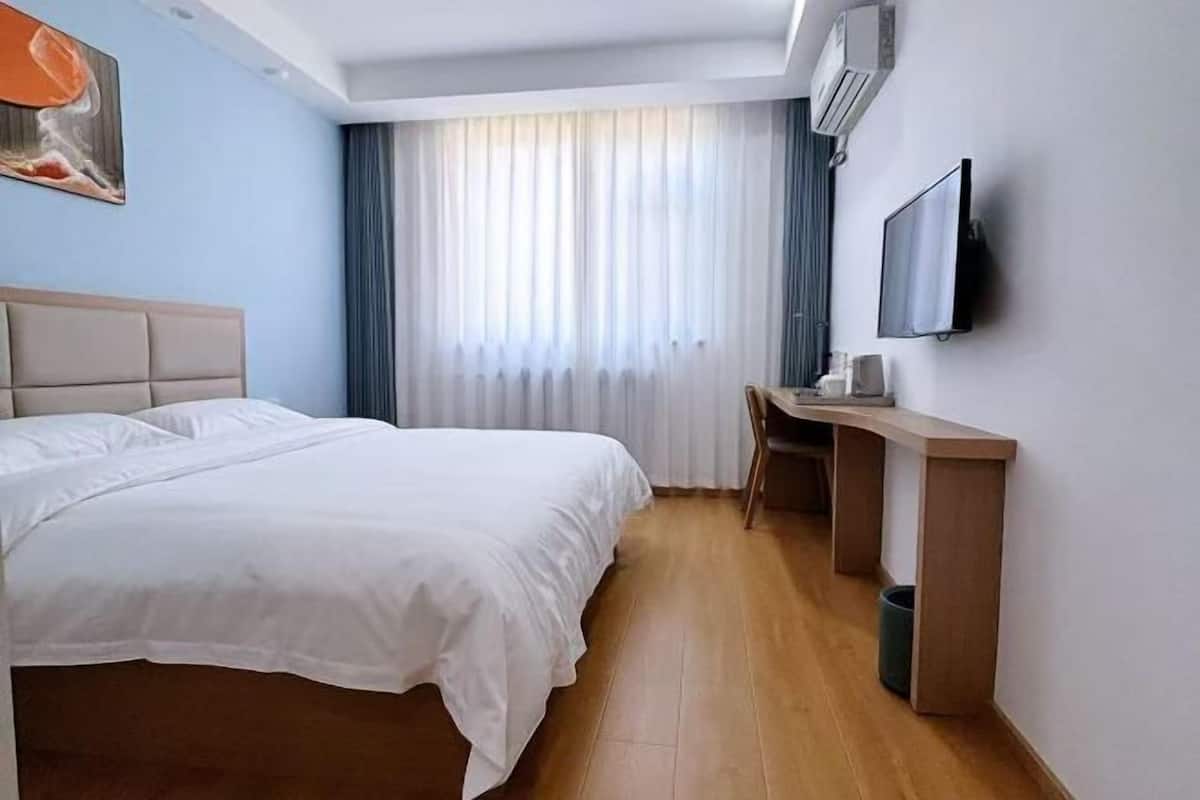 Habitació d'hotel amb llit, escriptori, televisió i finestra amb cortines.