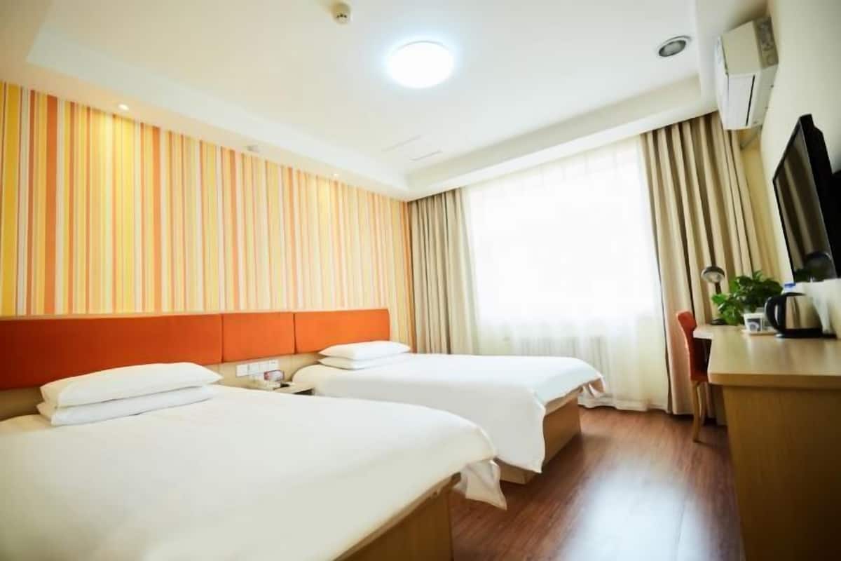 Habitació d'hotel amb dos llits, una taula de treball, una cadira, un televisor i una finestra amb cortines.