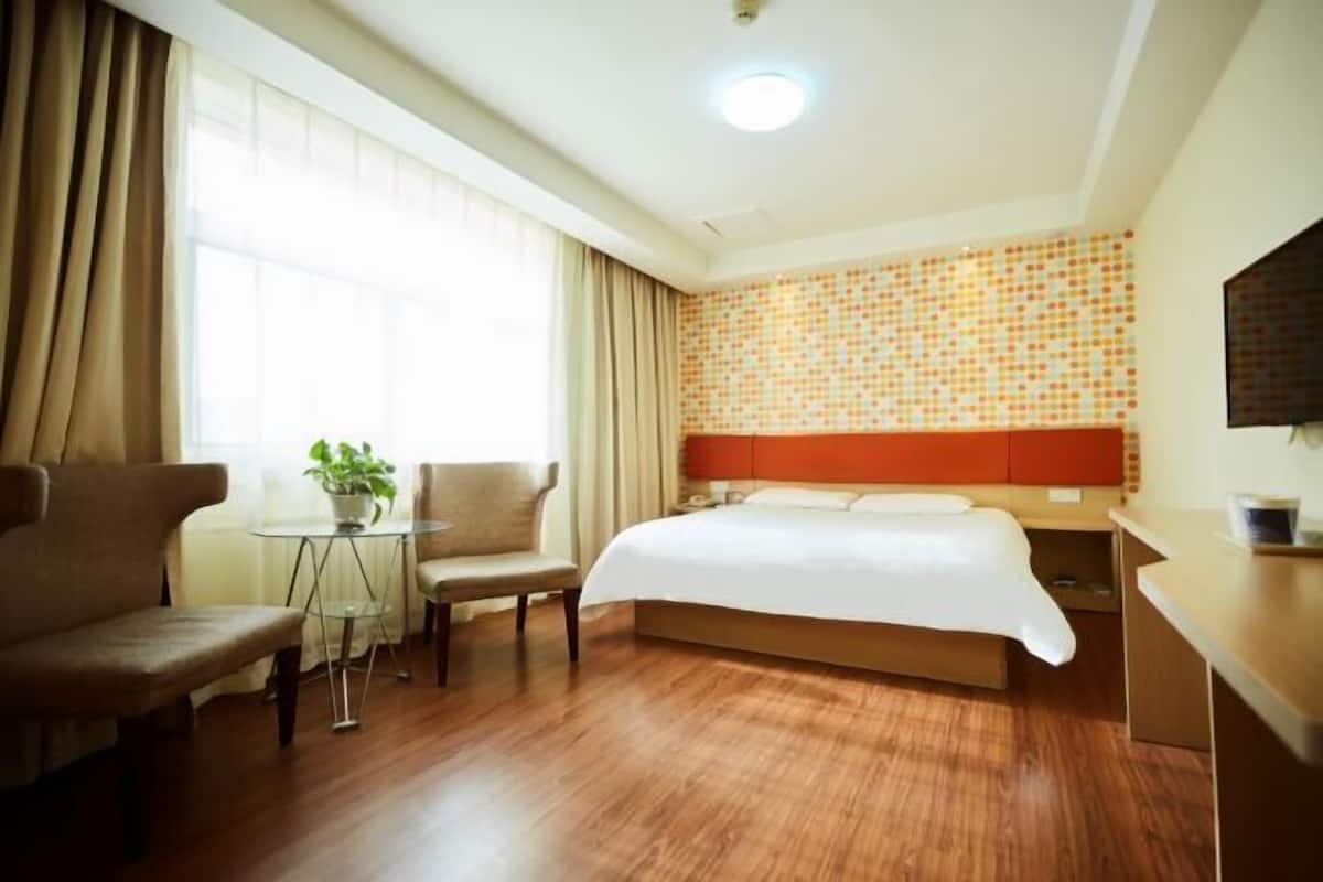 Habitació d'hotel amb llit, escriptori, cadira, taula petita amb una planta i finestra amb cortines.