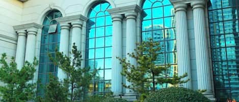 Un edificio con grandes ventanales arqueados y columnas, rodeado de vegetación cuidada.