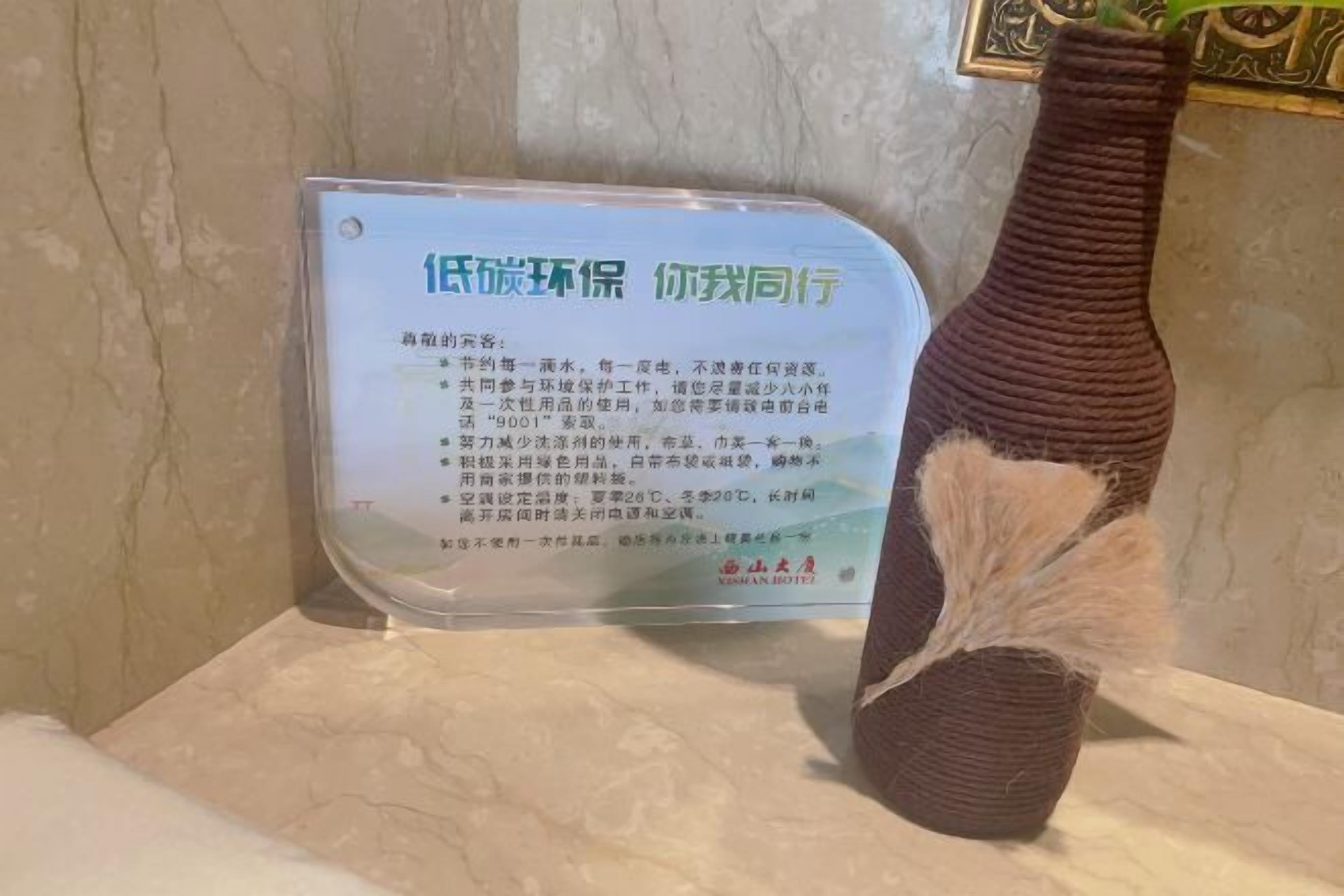 A sign with text in Chinese, placed on a marble surface next to a decorative brown vase with a feather.