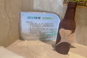 A sign with text in Chinese, placed on a marble surface next to a decorative brown vase with a feather. - Xishan Hotel (Taiyuan)