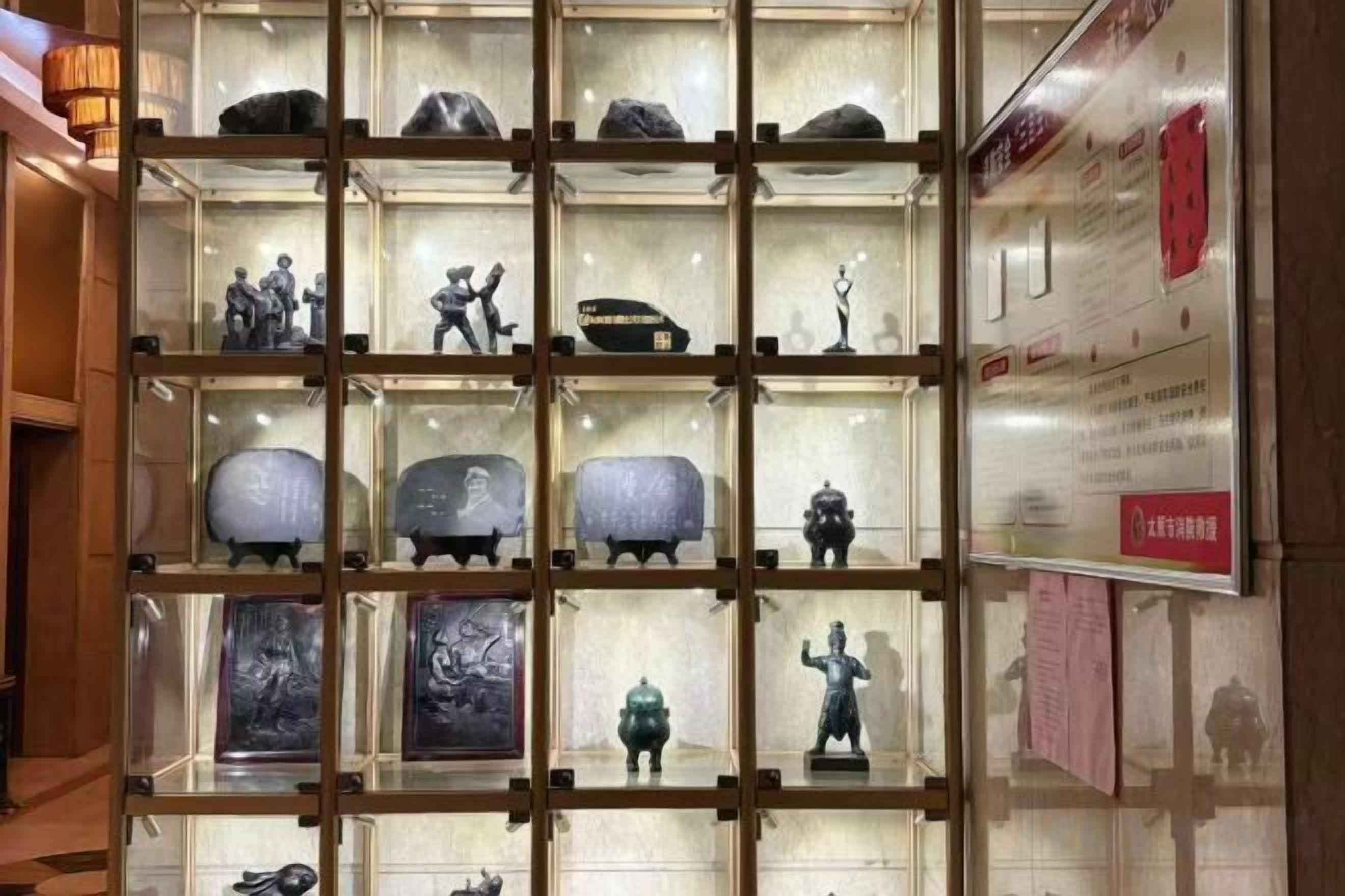 A display of various sculptures and artworks in a glass case, with informational plaques on the wall.