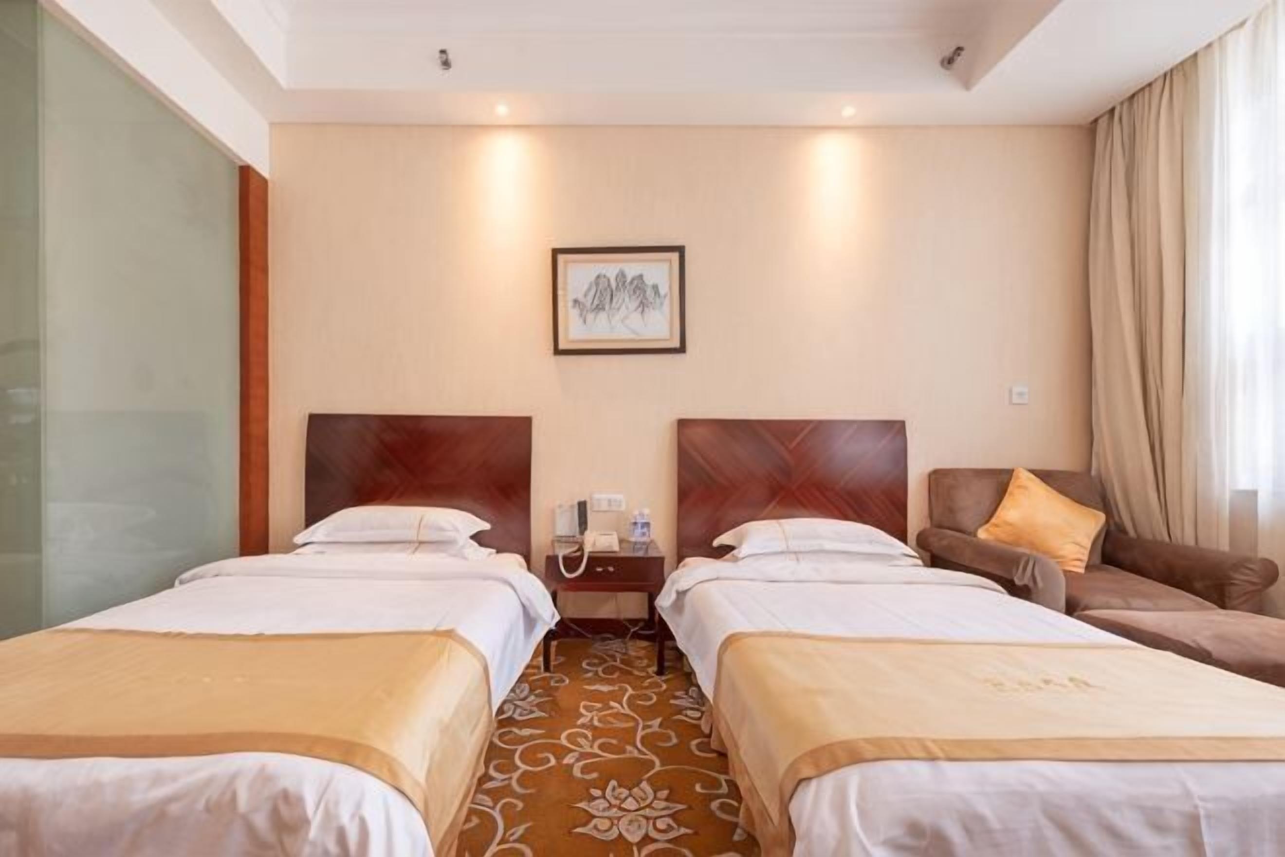 A hotel room with two beds, a sofa, a telephone, and a framed picture on the wall.