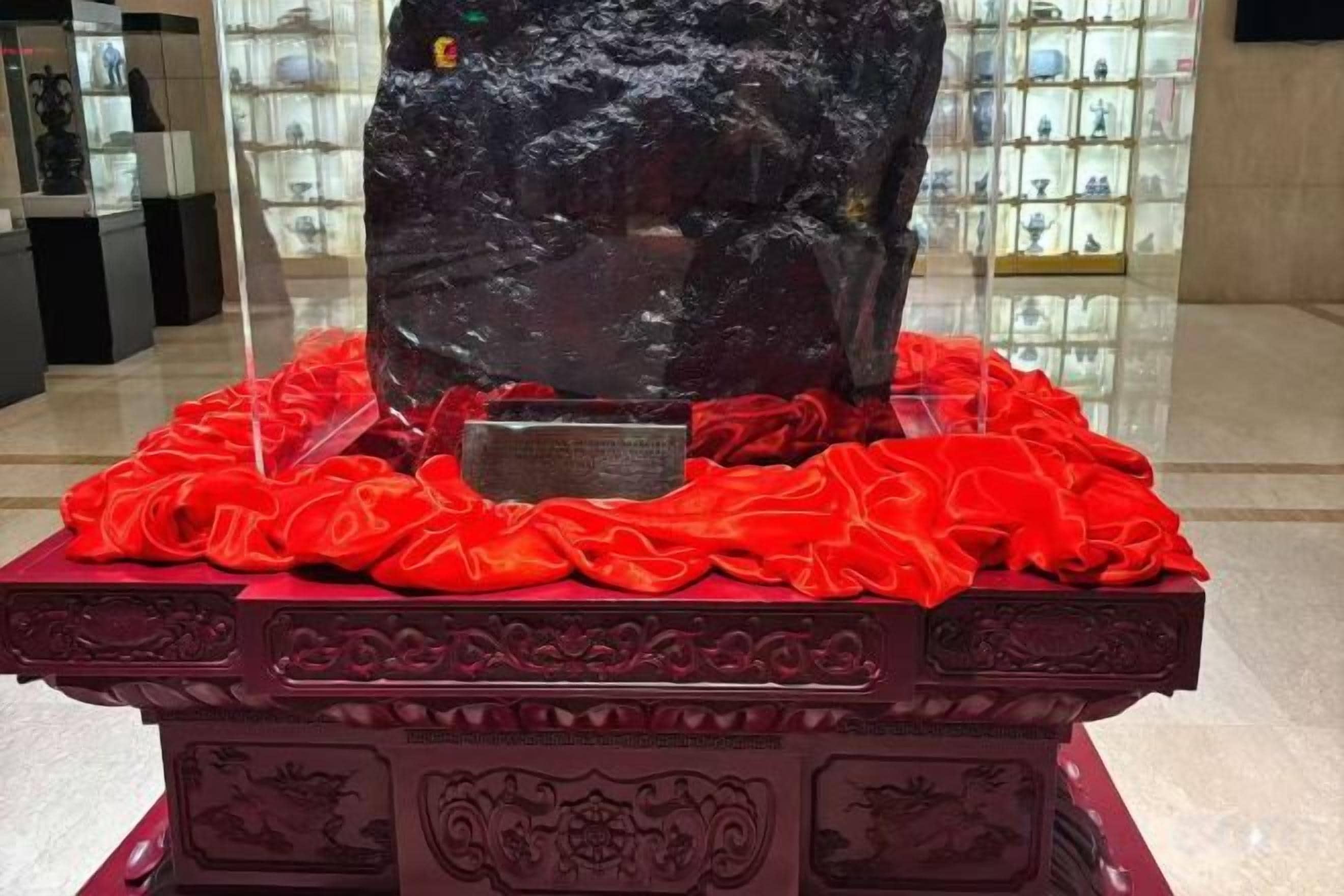 A display case with a dark object, surrounded by red fabric, on a decorative base.