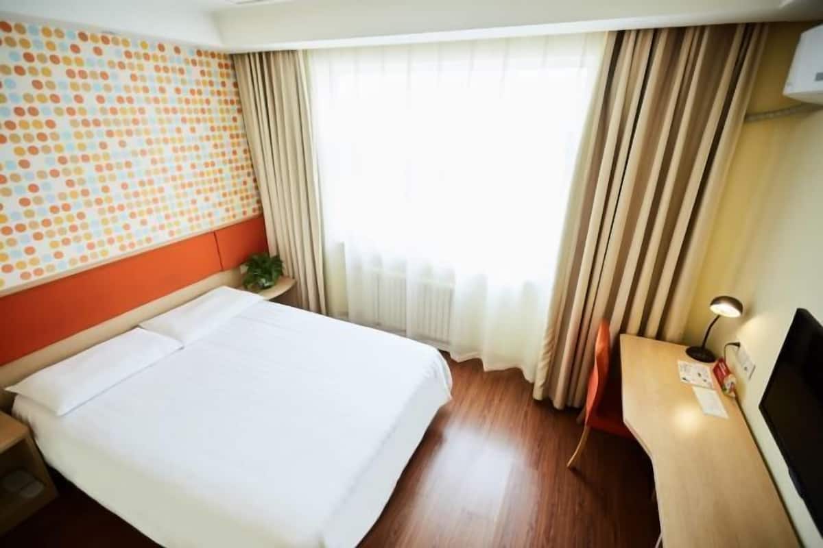 Habitació d'hotel amb llit, escriptori, finestra amb cortines i paret amb un disseny de punts.