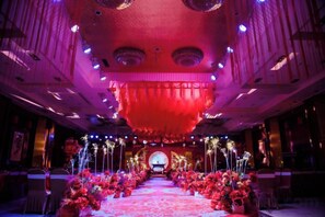 An indoor venue with a central aisle flanked by floral arrangements and a large, circular, illuminated structure above. - Xishan Hotel (Taiyuan)