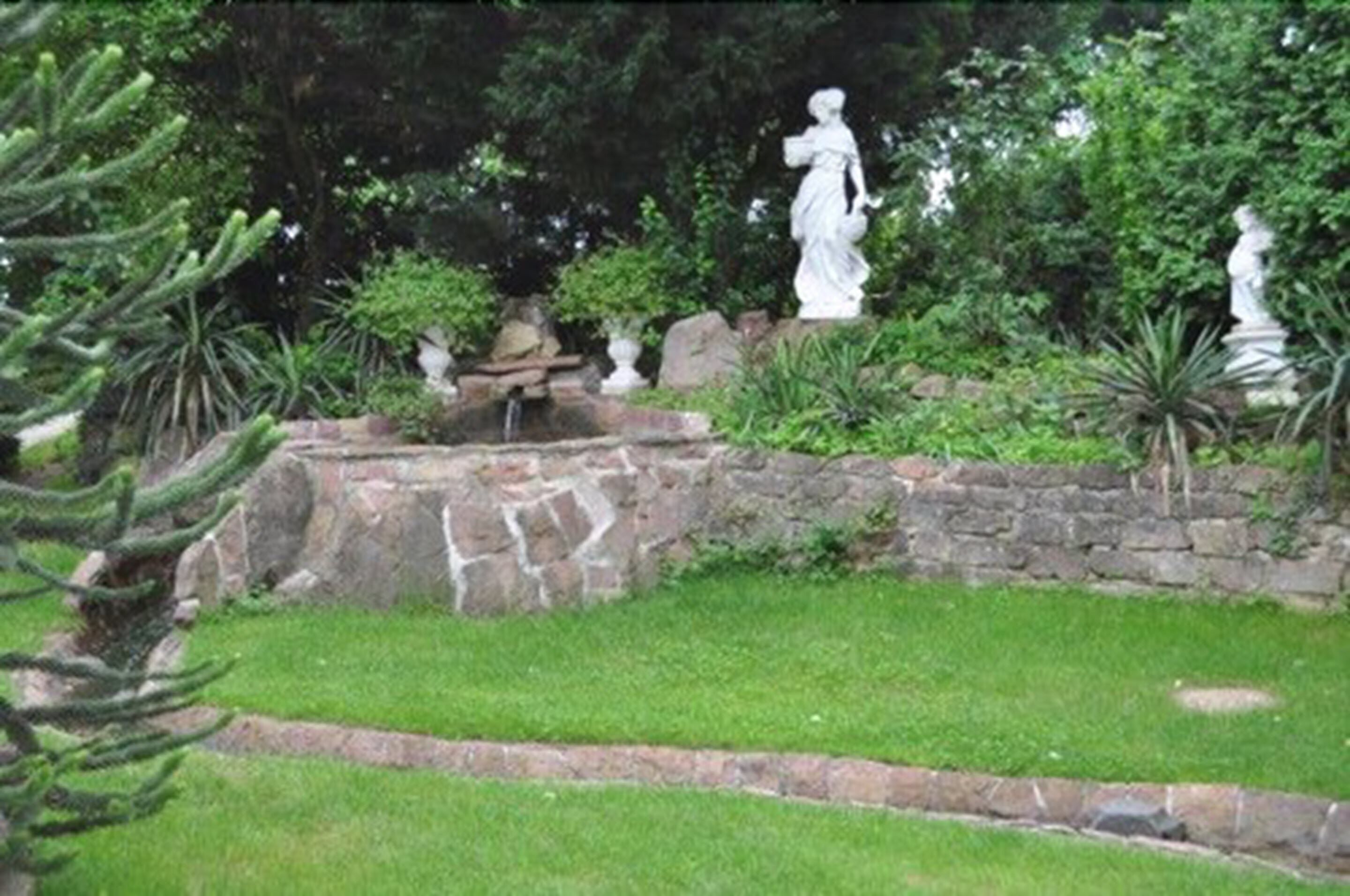 Un jardín con estatuas, un muro de piedra y una pequeña fuente.