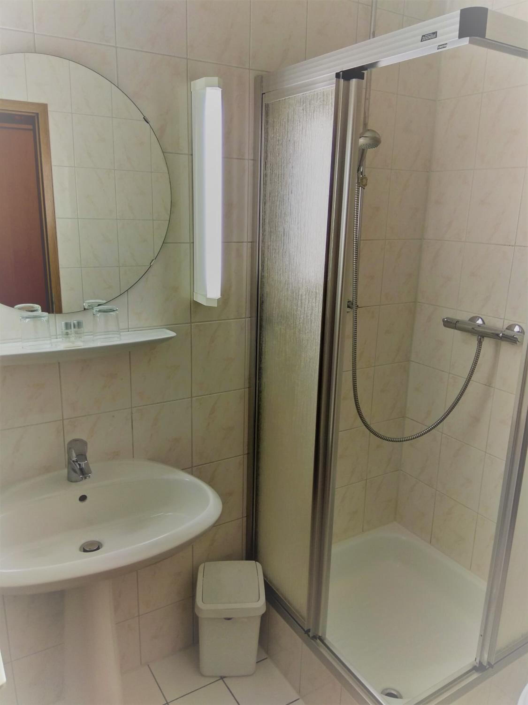 A bathroom with a glass-enclosed shower, a sink, a mirror, and a trash bin.