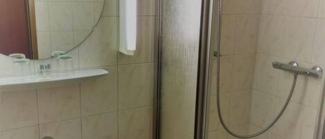 A bathroom with a glass-enclosed shower, a sink, a mirror, and a trash bin.