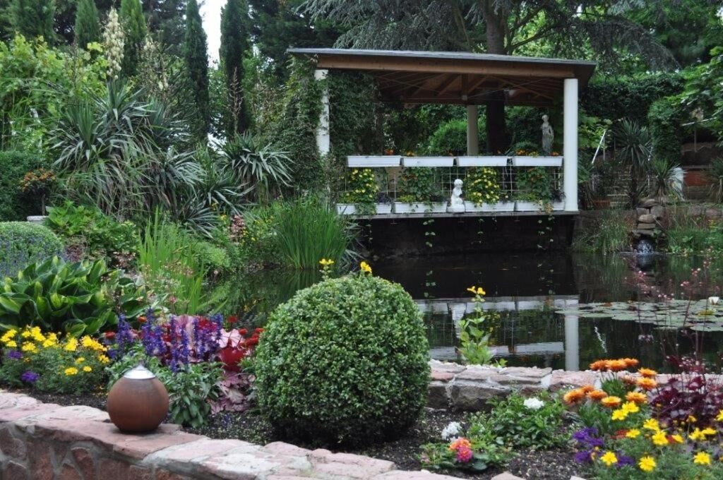 Un giardino con uno stagno, un gazebo e diverse piante e fiori.