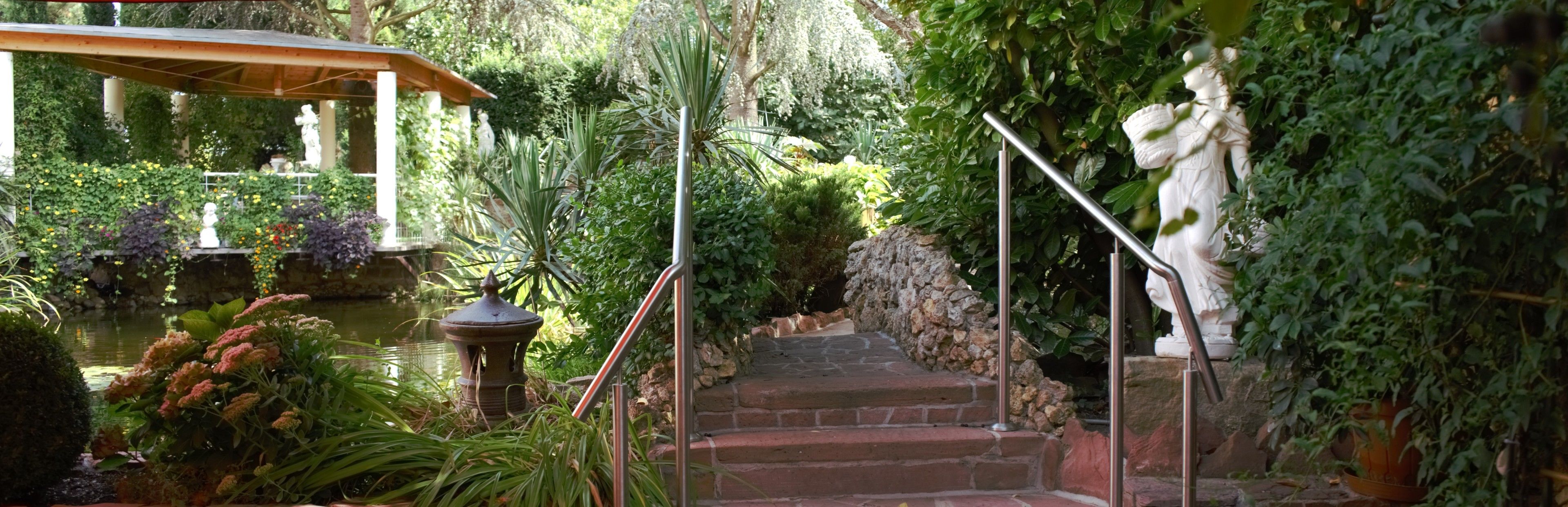 Un jardín con un estanque, estatuas y una escalera de piedra.