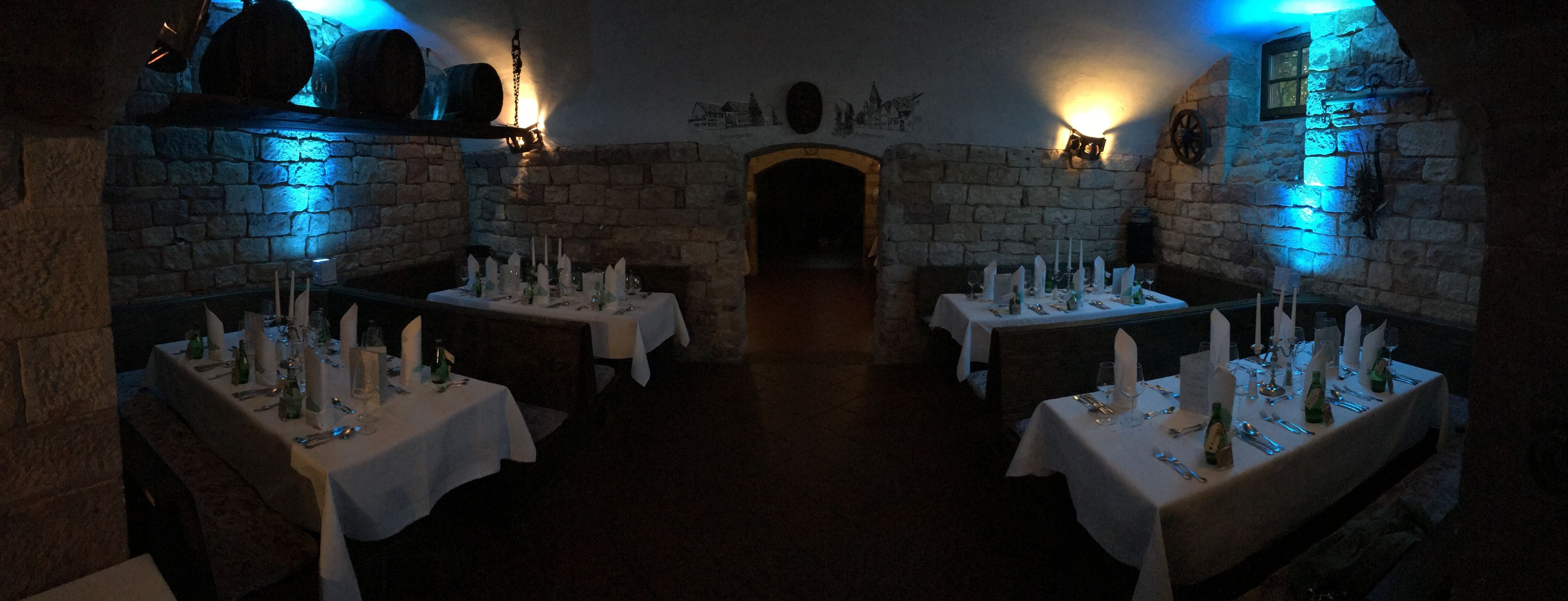 A dimly lit dining area with stone walls and tables set for a meal.