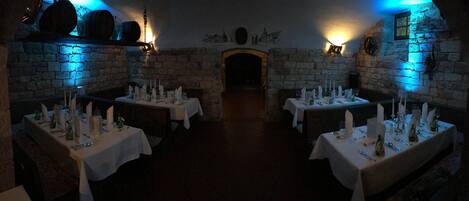 A dimly lit dining area with stone walls and tables set for a meal.