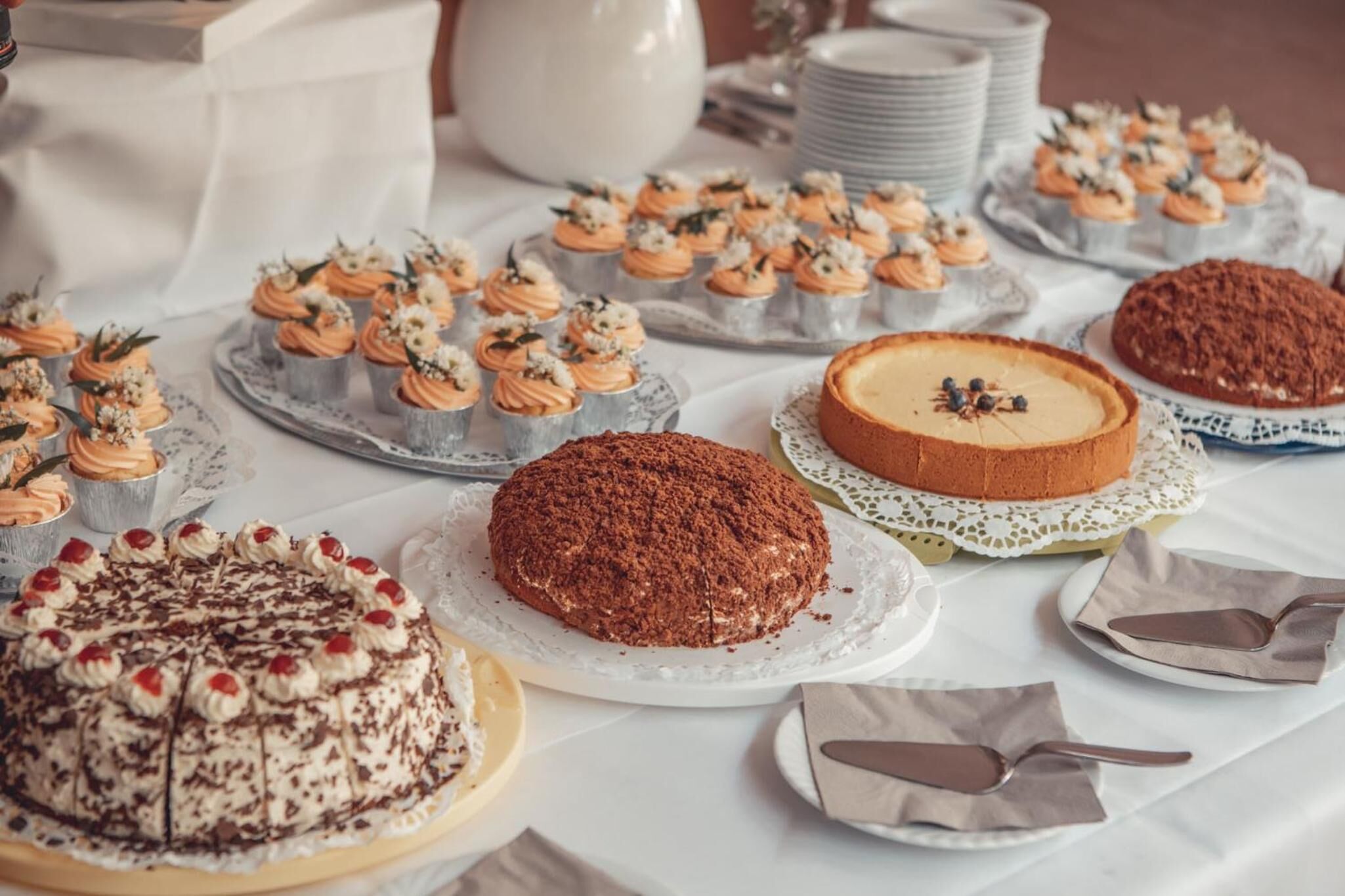Una mesa con diversos postres, como cupcakes, pastel de chocolate y pastel de queso.