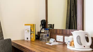 Habitación de hotel con escritorio de madera, cafetera, hervidor de agua, botella de agua, bloc de notas y caja con el menú de desayuno.