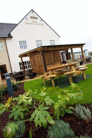 A building with a sign reading 'MARSTON'S THE CHAIN RUNNER' and a wooden outdoor seating area with tables and benches.