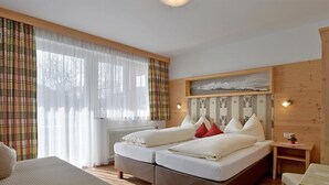 A hotel room with two beds, a large window with sheer curtains, a wooden headboard, and a small table with a lamp. - Quadruple room with bath, WC - the Christophorus (Soell)