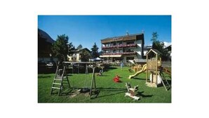 A playground with a swing set and slides, a small wooden structure, and a building with balconies in the background. - Quadruple room with bath, WC - the Christophorus (Soell)