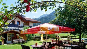 An outdoor seating area with tables and chairs, a red umbrella, and a building in the background. - Quadruple room with bath, WC - the Christophorus (Soell)