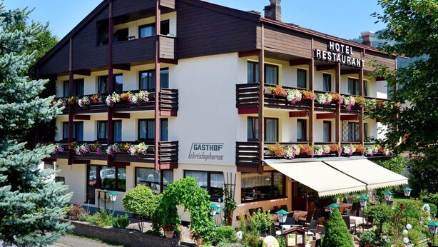 A hotel with a restaurant, featuring balconies with flower boxes, outdoor seating, and a garden area. - Quadruple room with bath, WC - the Christophorus (Soell)