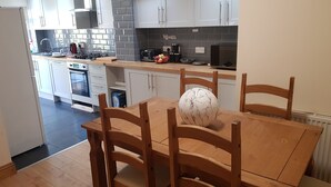 A modern kitchen with white cabinets, a tiled backsplash, and a wooden dining table with chairs. - Oxford City Guest House (Oxford)