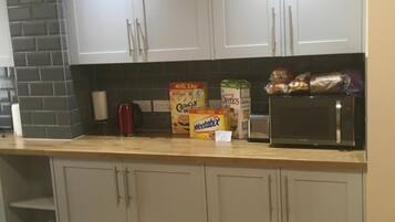 A kitchen with white cabinets, a microwave, and cereal boxes on the counter.