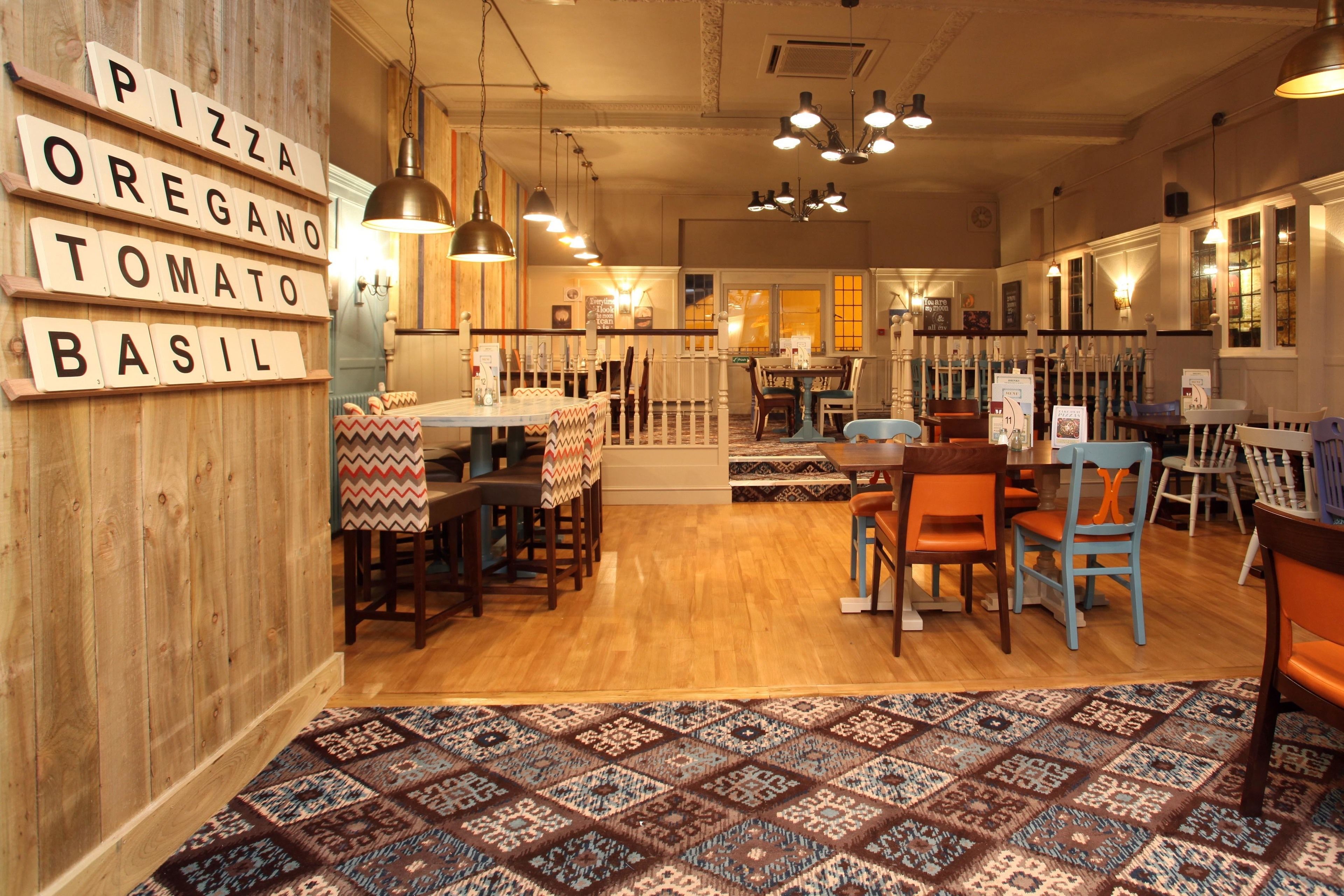 Un acogedor interior de restaurante con paredes de madera, un tapete estampado y diferentes opciones de asientos, incluidas mesas y sillas.