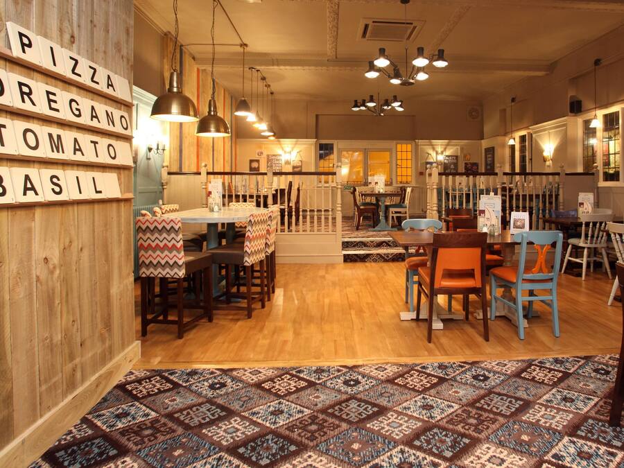 Un acogedor interior de restaurante con paredes de madera, un tapete estampado y diferentes opciones de asientos, incluidas mesas y sillas.
