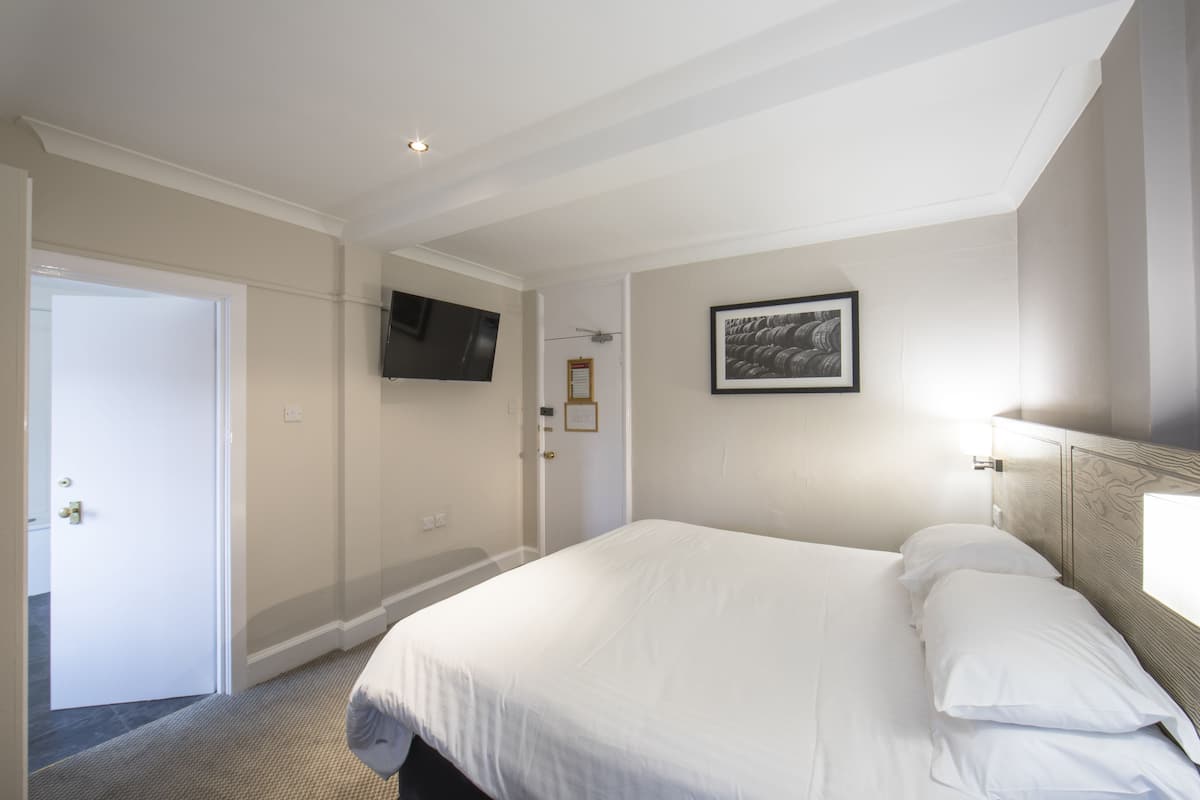A hotel room with a large bed, a flat-screen TV mounted on the wall, and a framed picture above the bed.