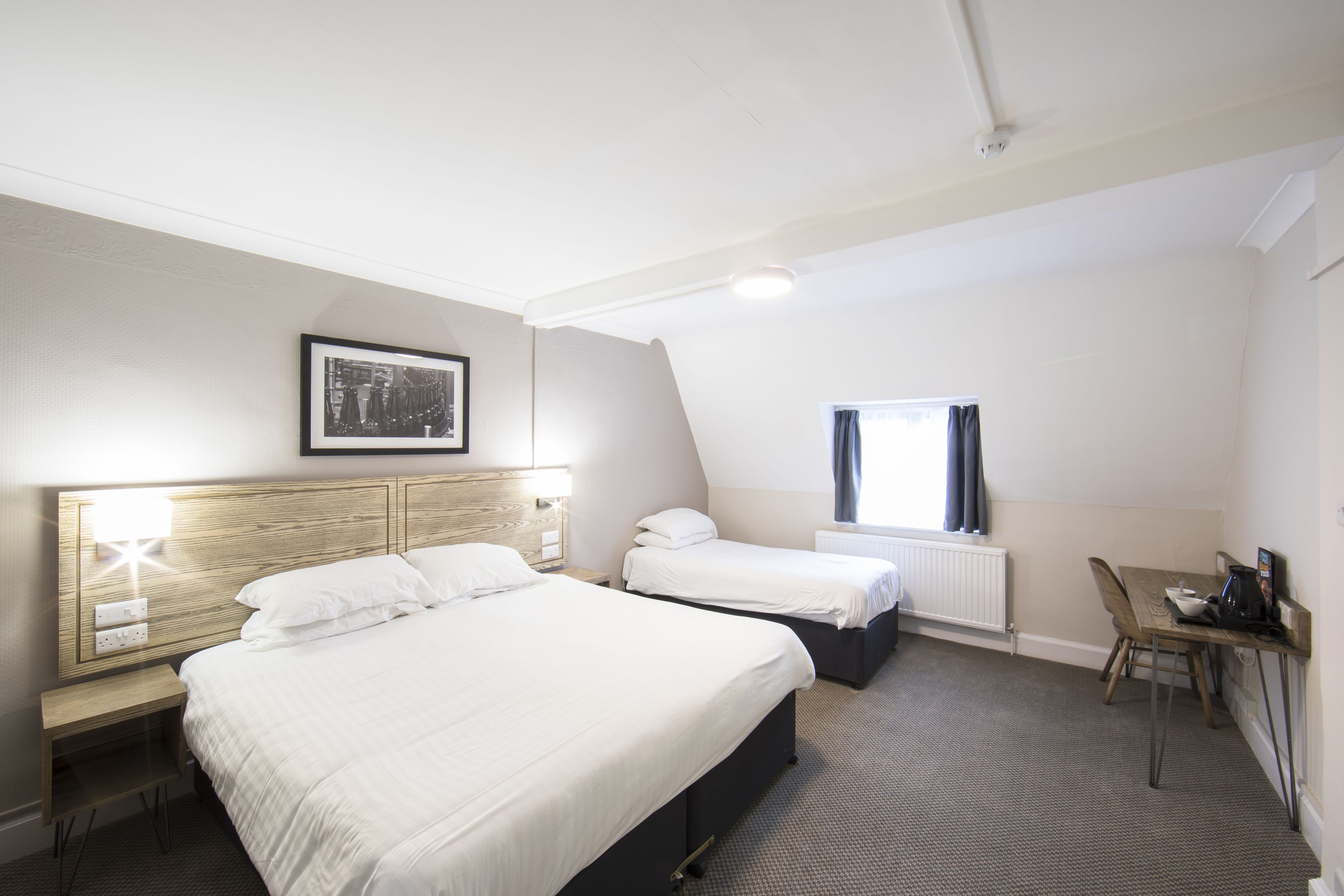 A hotel room with a large bed, a smaller bed, a desk, and a window with curtains.