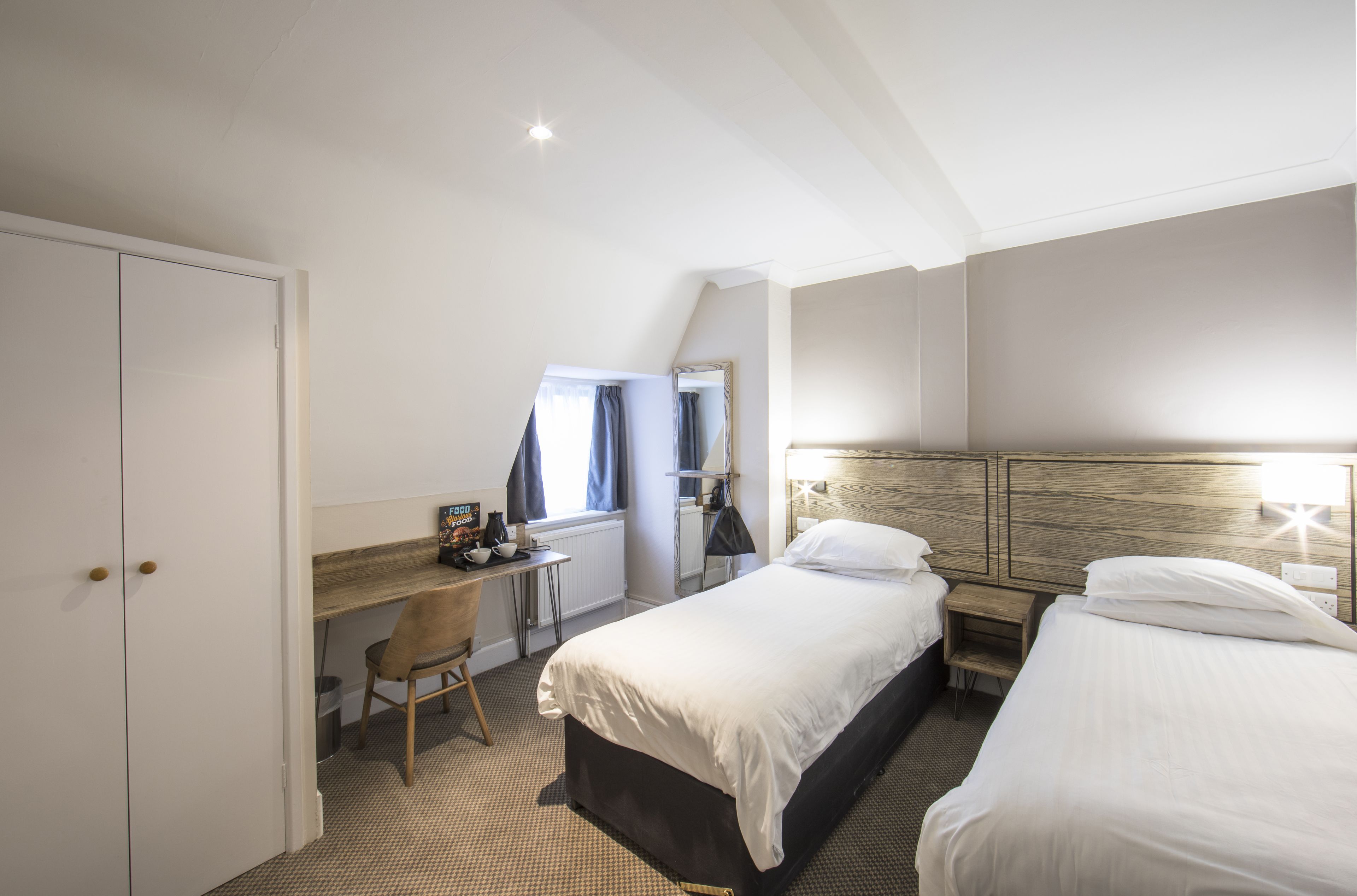 A hotel room with a bed, a desk, a chair, and a wardrobe.