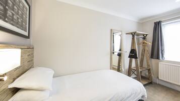 Habitación de hotel con cama, cabecero de madera, lámpara colgante, espejo, radiador y ventana con cortinas.