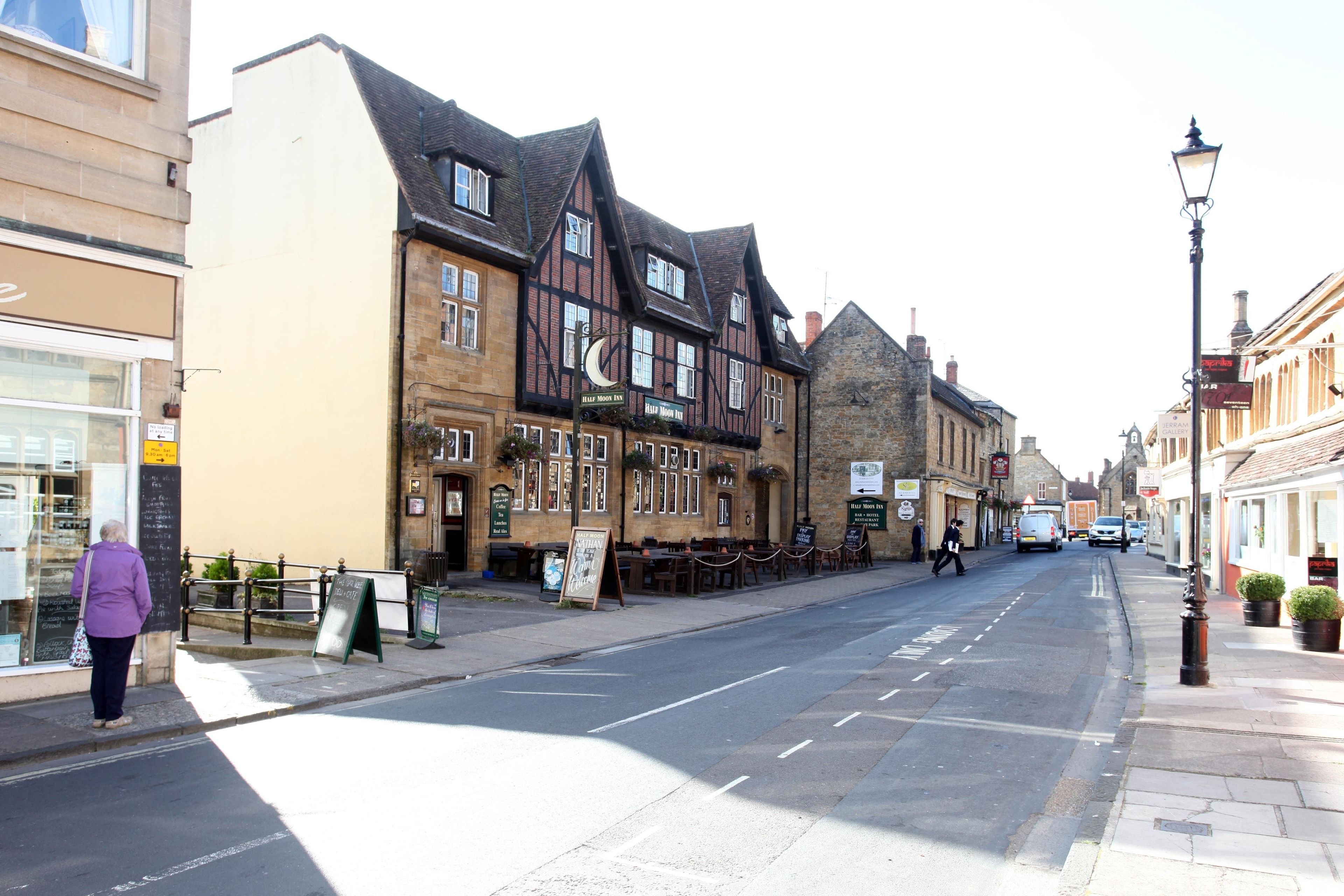 A street with traditional architecture, including a pub with outdoor seating and a signboard.