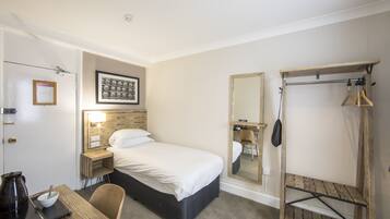 Una habitación de hotel con cama, mesita de noche, silla y una estantería de madera.