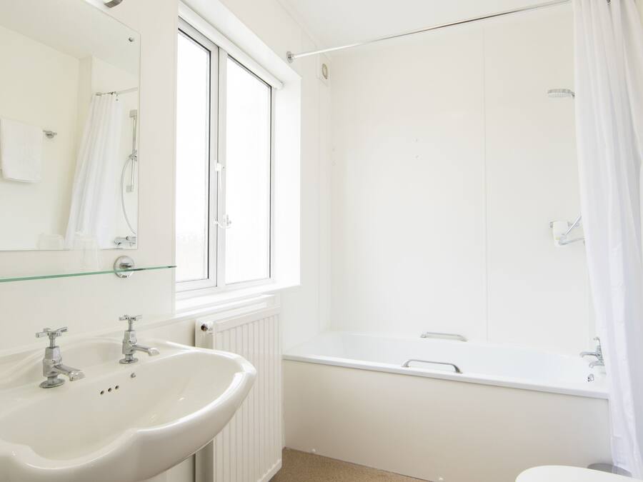 Un baño con lavamanos blanco, espejo e inodoro. Hay una ventana, cortina de ducha y bañera.