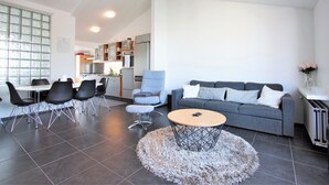 A modern living room with a grey sofa, round coffee table, and black chairs. A kitchen is visible in the background with a fridge and oven. - Odinn Reykjavik Odinsgata Apartments (Reykjavik)