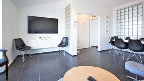 A modern hotel lobby with a flat-screen TV mounted on the wall, black chairs arranged around a wooden table, and a large window with a view of trees. - Odinn Reykjavik Odinsgata Apartments (Reykjavik)
