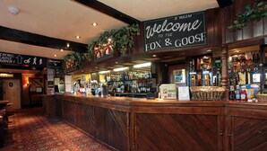 A bar area with a wooden counter, shelves with bottles, and a welcome sign. - Fox & Goose, Barrow Gurney by Marston's Inns (Bristol)