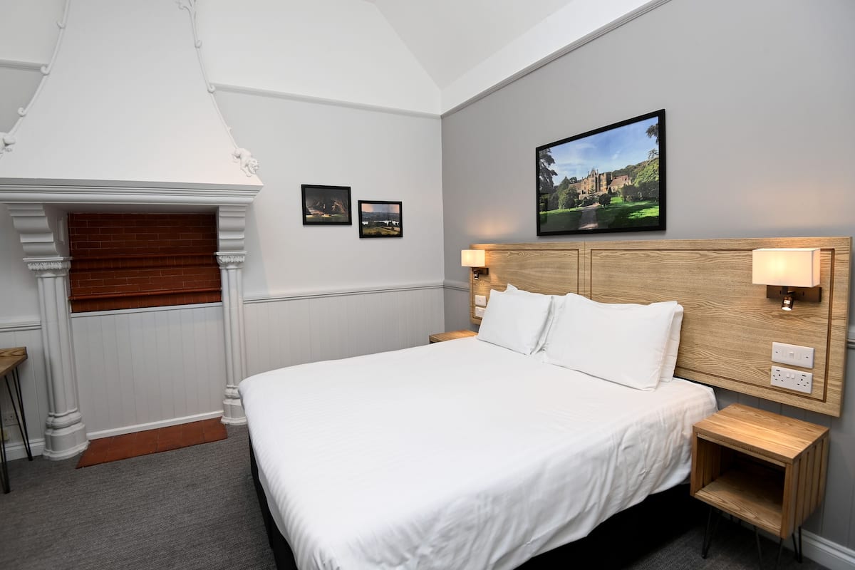A neatly arranged hotel room with a large bed, two bedside tables with lamps, a small table, and a fireplace.