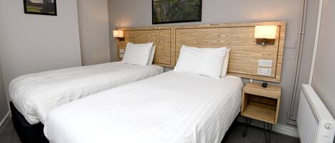 Habitación de hotel con dos camas individuales, cabecero de madera, lámparas de noche, mesitas de noche de madera y un cuadro en la pared.