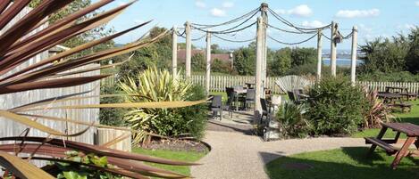 A garden patio with a gravel path leading to a seating area with tables and chairs.