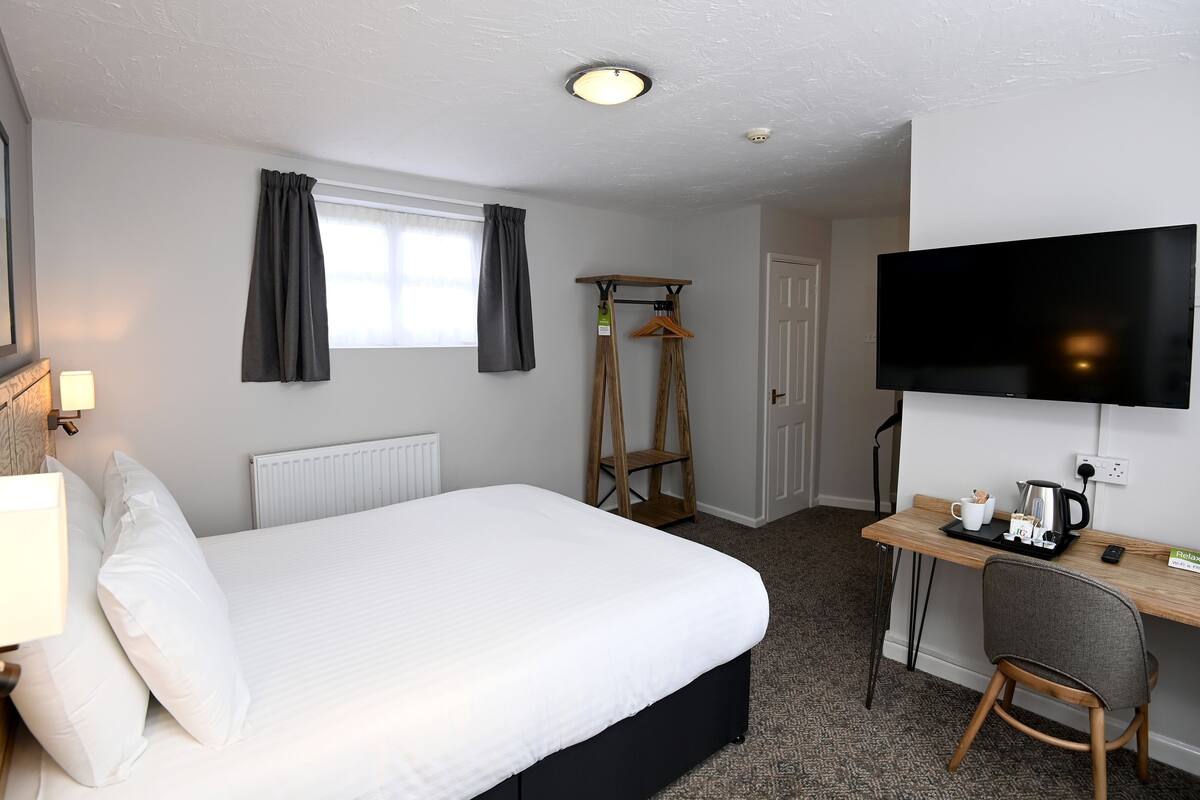 A hotel room with a bed, a desk with a chair, a television, and a radiator.