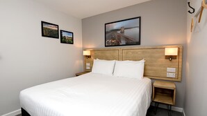 A neatly made bed with white linens, two bedside tables with lamps, and two framed pictures on the wall. - Fox & Goose, Barrow Gurney by Marston's Inns (Bristol)